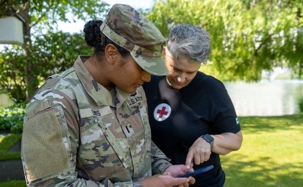 A Red Cross volunteer points something out on the phone of a uniformed servicemember.